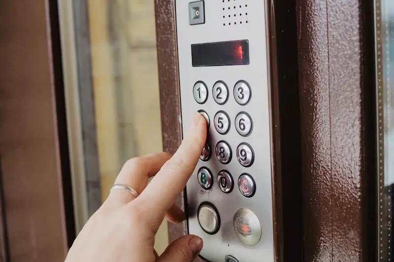 Hand tippt auf Zahlentastatur eines Zutrittskontrollsystems an einer Tür mit braunem Rahmen